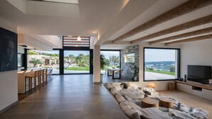 A spacious living area with a large sofa, a dining area with chairs, a television, and a view of the outdoors. - Luxury Villa West Nice (Nice)