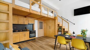 Una cucina moderna con mobili in legno, una zona pranzo con sedie gialle e un televisore montato a parete.