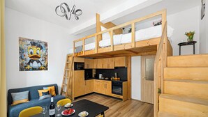 Una camera da letto in stile loft con una cuccetta, un'area pranzo con tavolo e sedie, una cucina con pensili in legno e un quadro appeso al muro.