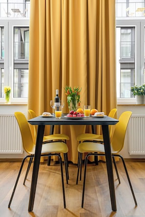 A dining area with a table set for two, yellow chairs, a bottle of wine, glasses, and fresh fruit. - Urban Loft Apartment (Brno)