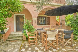 An outdoor patio with a table and chairs, a black umbrella, and a stone-tiled floor. - Astrakeri Gardens Villa (Corfu)