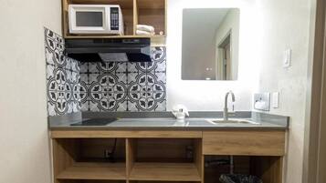 A small kitchenette with a microwave, sink, and wooden shelves.