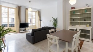 Un salon moderne comprenant un canapé, une table à manger, des chaises, un téléviseur et une bibliothèque.