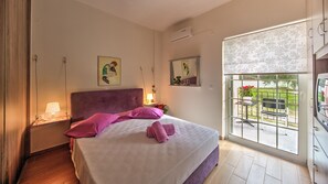 Ein Schlafzimmer mit einem großen Bett, einem Nachttisch, einem Fenster mit Blick nach draußen und einer Wand-Klimaanlage.