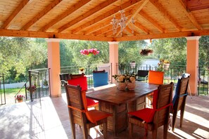 Eine Holzterrasse im Freien mit Tisch und Stühlen, umgeben von Topfpflanzen und einem Geländer.