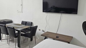 Une pièce dotée d’un téléviseur à écran plat fixé au mur, d’une table à manger avec des chaises et d’une petite table d’appoint en bois.