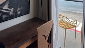 Ein Zimmer mit einem großen, abstrakten Gemälde, einem Holztisch, einem Stuhl und Blick auf das Meer durch eine Glastür.