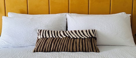 A bed with white textured bedding, a patterned pillow, and a yellow headboard.