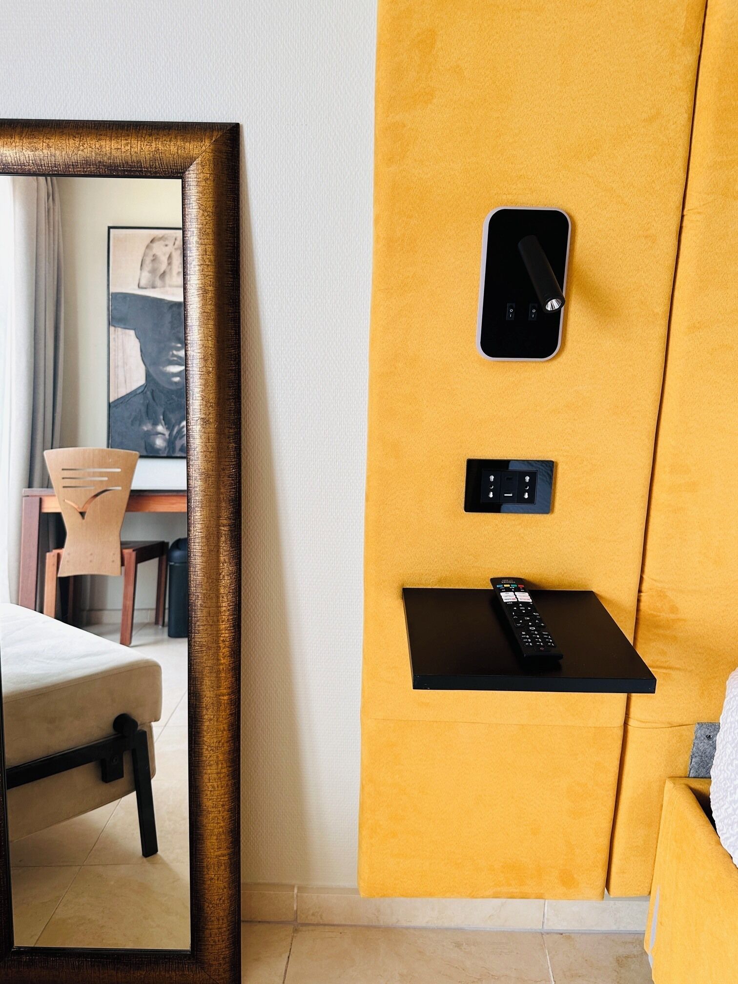 Une chambre d’hôtel avec un grand miroir, un téléviseur fixé au mur, une télécommande et une petite étagère.
