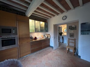 A kitchen with wooden cabinets, a microwave, and an oven. There is a door leading to another room with a clock on the wall. - Secluded Chianti Estate with Infinity Pool in the Hills of Siena (Toscana)