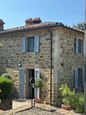 A stone building with a tiled roof, multiple windows with shutters, a door, and a small garden with potted plants. - Secluded Chianti Estate with Infinity Pool in the Hills of Siena (Toscana)