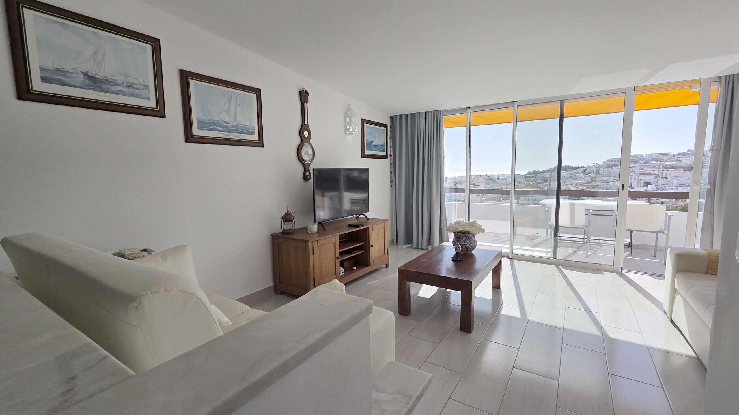 A living room with a sofa, TV, wooden cabinet, and a balcony with a view.