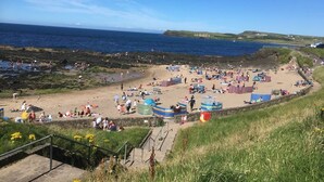 A coastal beach scene with people, tents, and a clear sky.