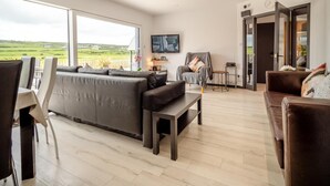 A spacious living room with a large window, a sofa, a TV, and a dining area.