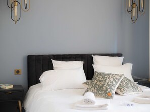 Een net opgemaakt bed met witte lakens, een donker hoofdbord en decoratieve kussens.