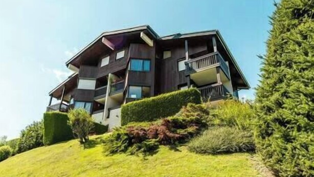 Un edificio moderno a più piani con balconi, immerso nel verde e circondato da alberi.
