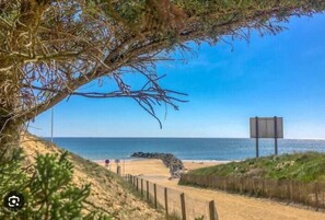 A beach with a wooden fence, a clear sky, and a large rock formation in the distance. - Spacious home near the sea and Clemenceau (Saint-Vincent-sur-Jard)