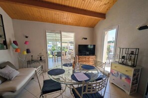 A living room with a glass table, sofa, TV, and a balcony view. - Spacious home near the sea and Clemenceau (Saint-Vincent-sur-Jard)