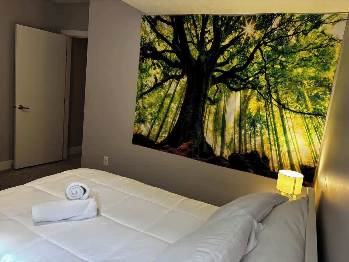 Une chambre d’hôtel avec un grand lit, un tableau représentant un arbre accroché au mur, une porte et une lampe de chevet.