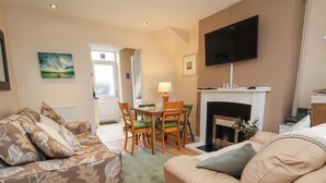 A living room with a sofa, a dining table with chairs, a fireplace, and a television mounted on the wall.