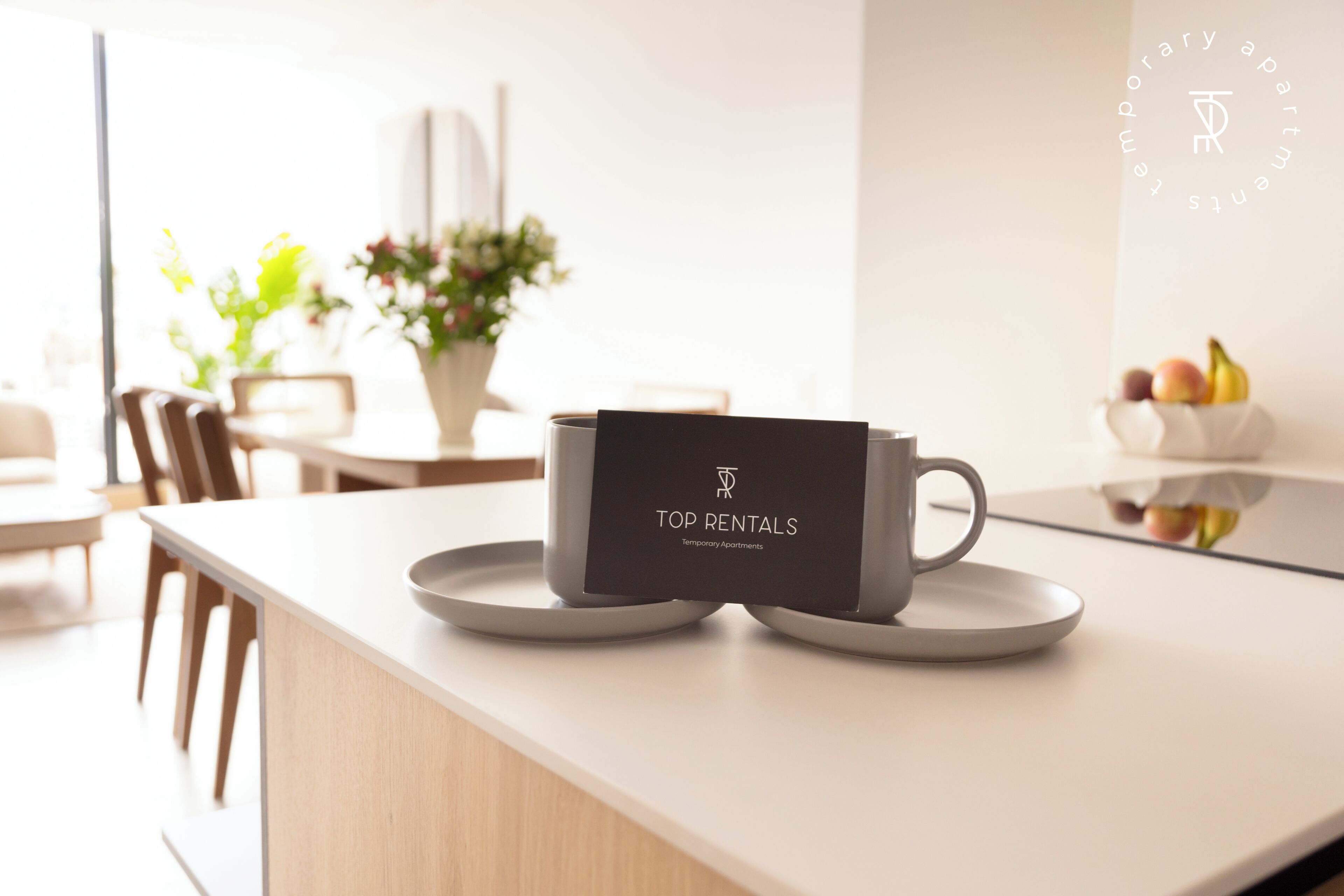 A modern kitchen with a coffee table holding a black mug and a placemat with 'TOP RENTALS' text.