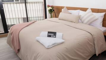 A neatly made bed with a welcome sign, a wooden headboard, and a view of a balcony with a railing.