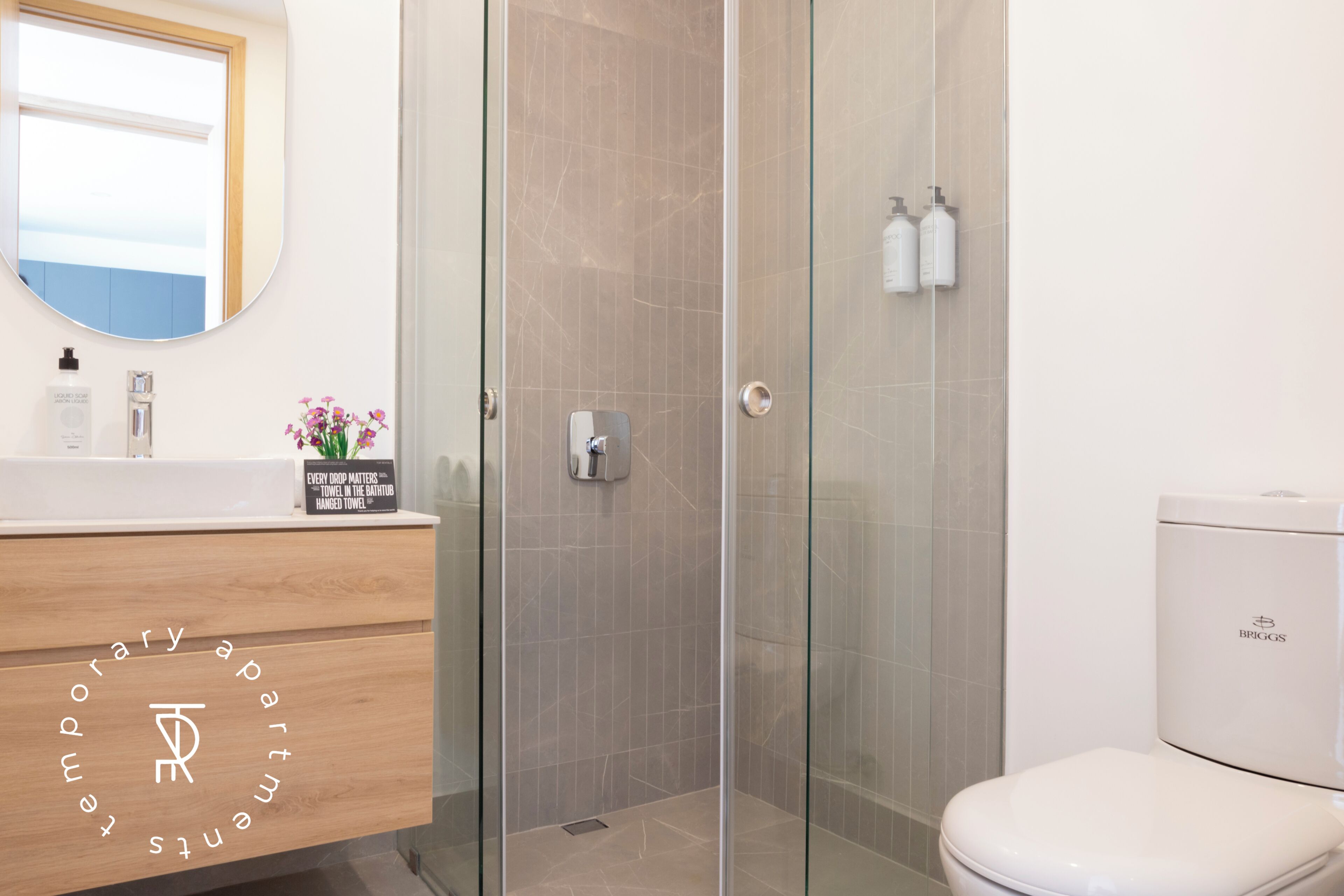 A modern bathroom with a glass shower enclosure, a wooden vanity with a mirror, and a white toilet.