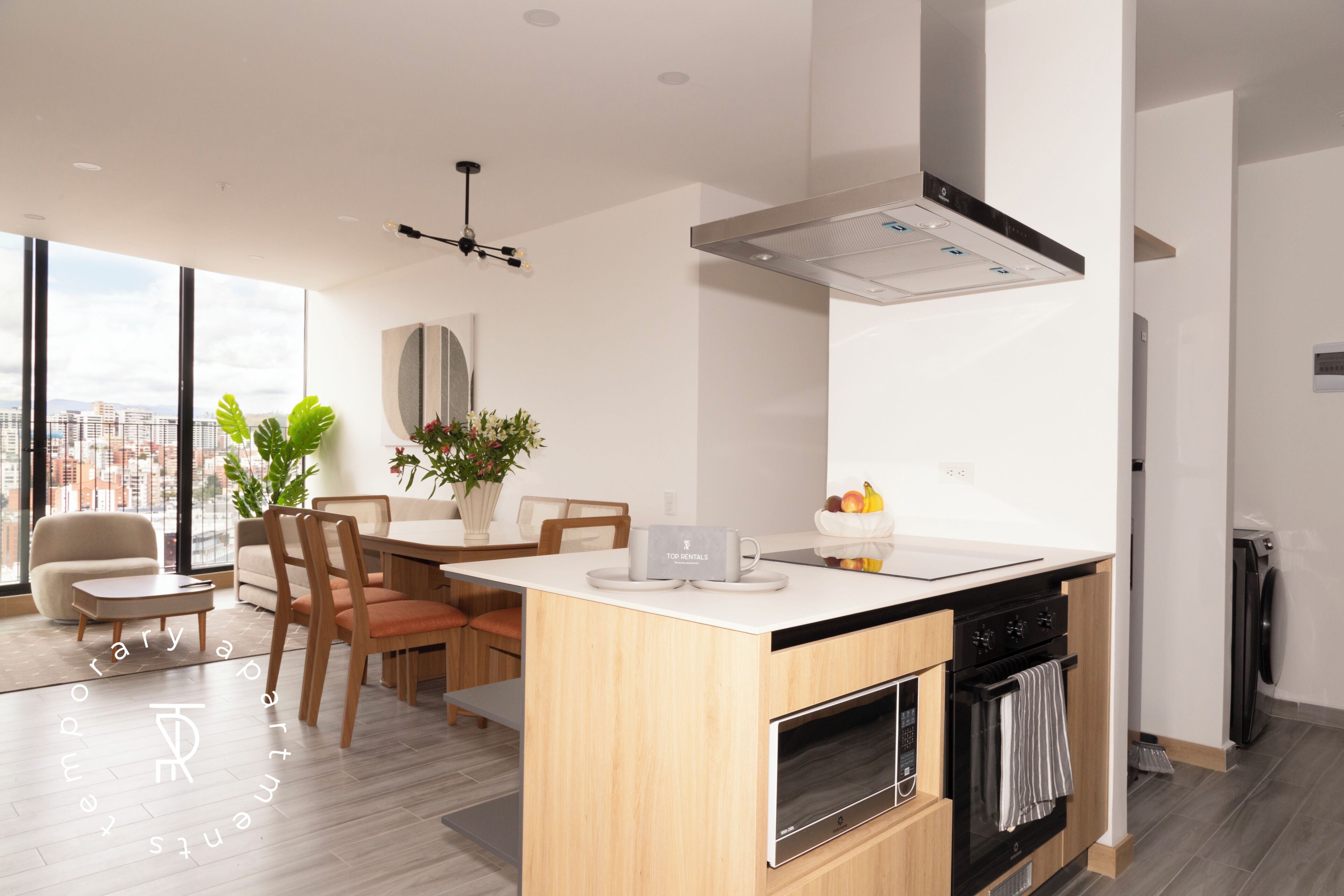 Una cocina moderna con una isla central, horno empotrado y comedor con vista a la ciudad.