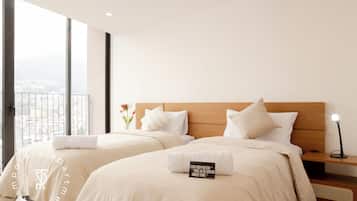 Ein Hotelzimmer mit zwei Betten, einem Nachttisch, einer Lampe und Blick auf die Stadt.