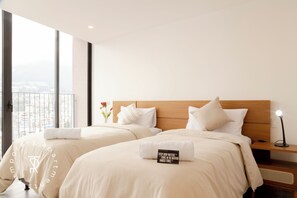 Una camera d'albergo con due letti, un comodino, una lampada e vista sulla città.