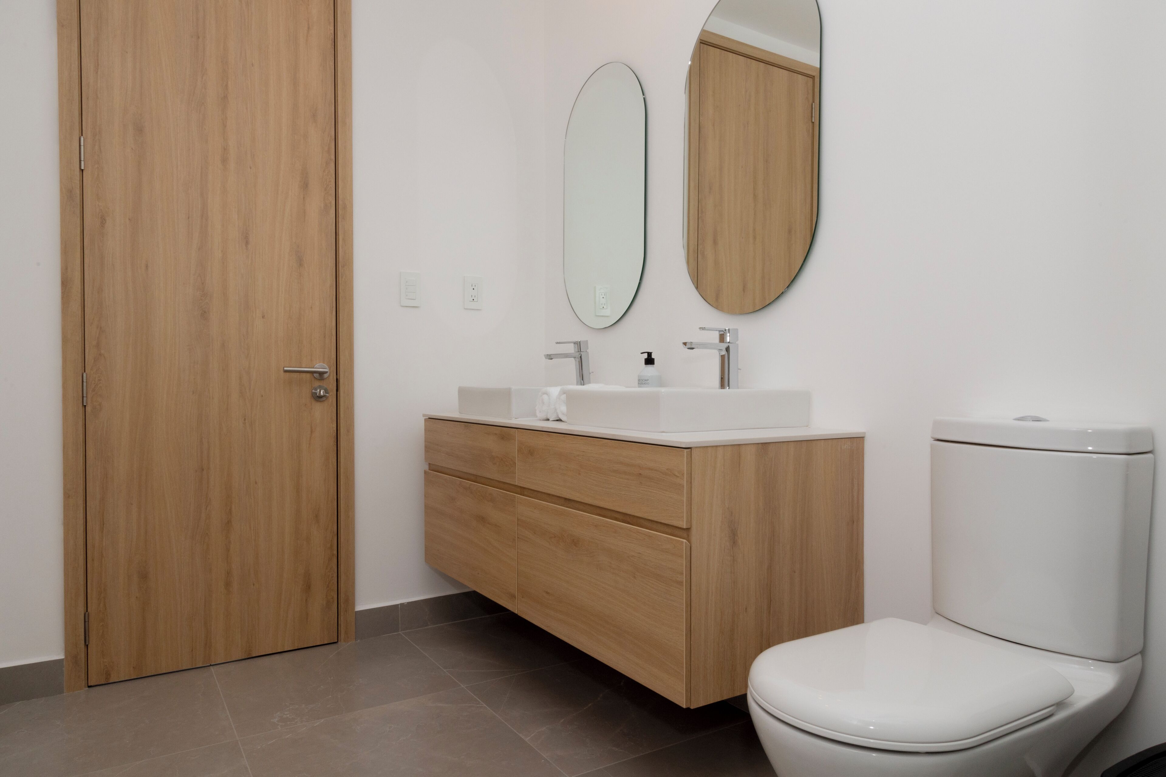A bathroom with a wooden door, a white toilet, a vanity with a mirror, and a sink.