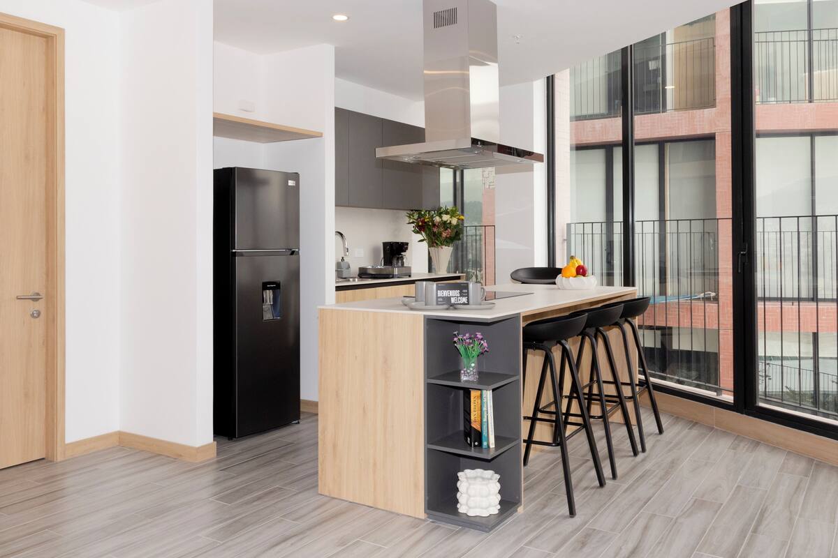 A modern kitchen with a built-in island, bar stools, and a large window offering a view.