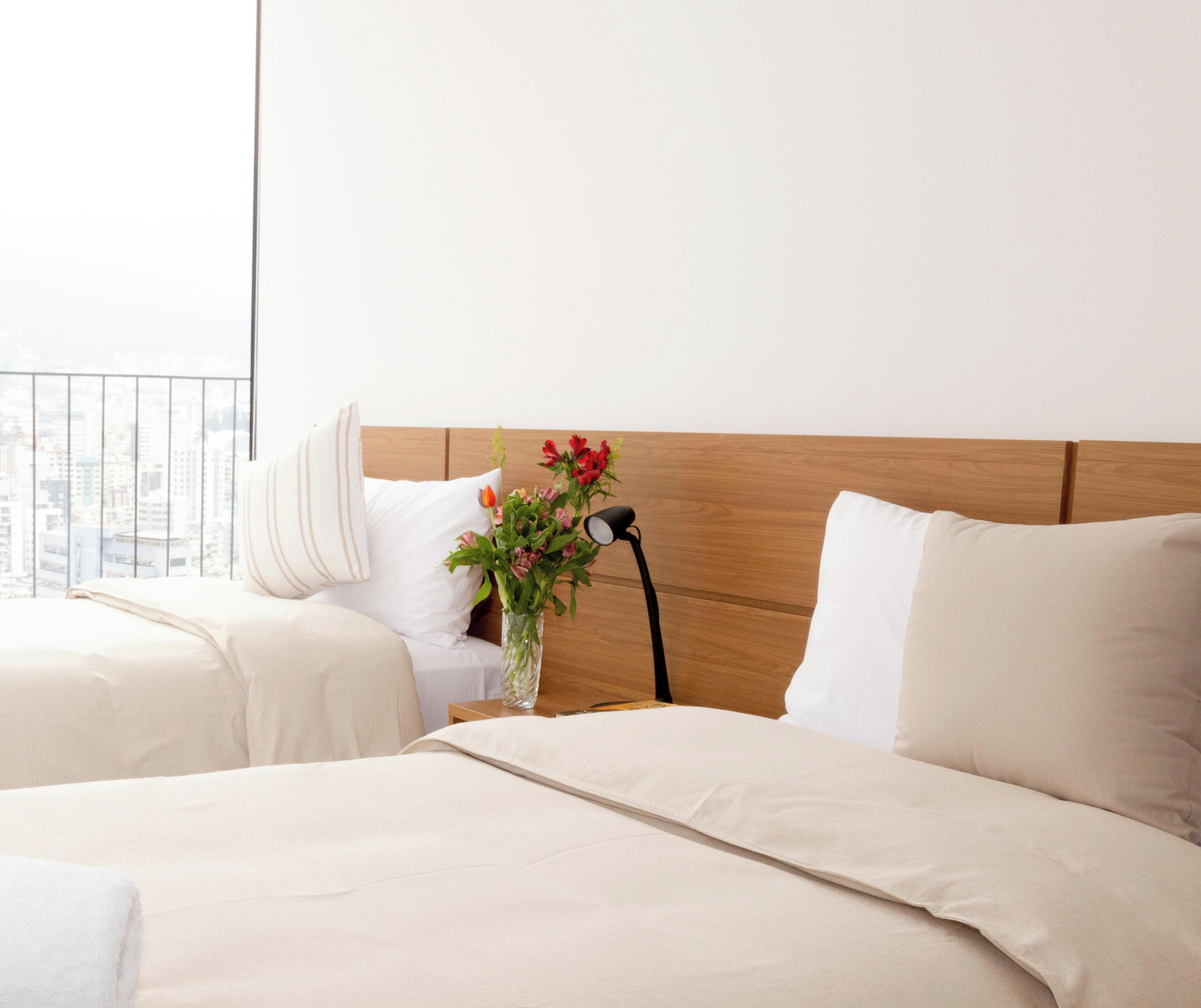 Una camera d'albergo con due letti, un comodino con una lampada e un vaso con fiori.