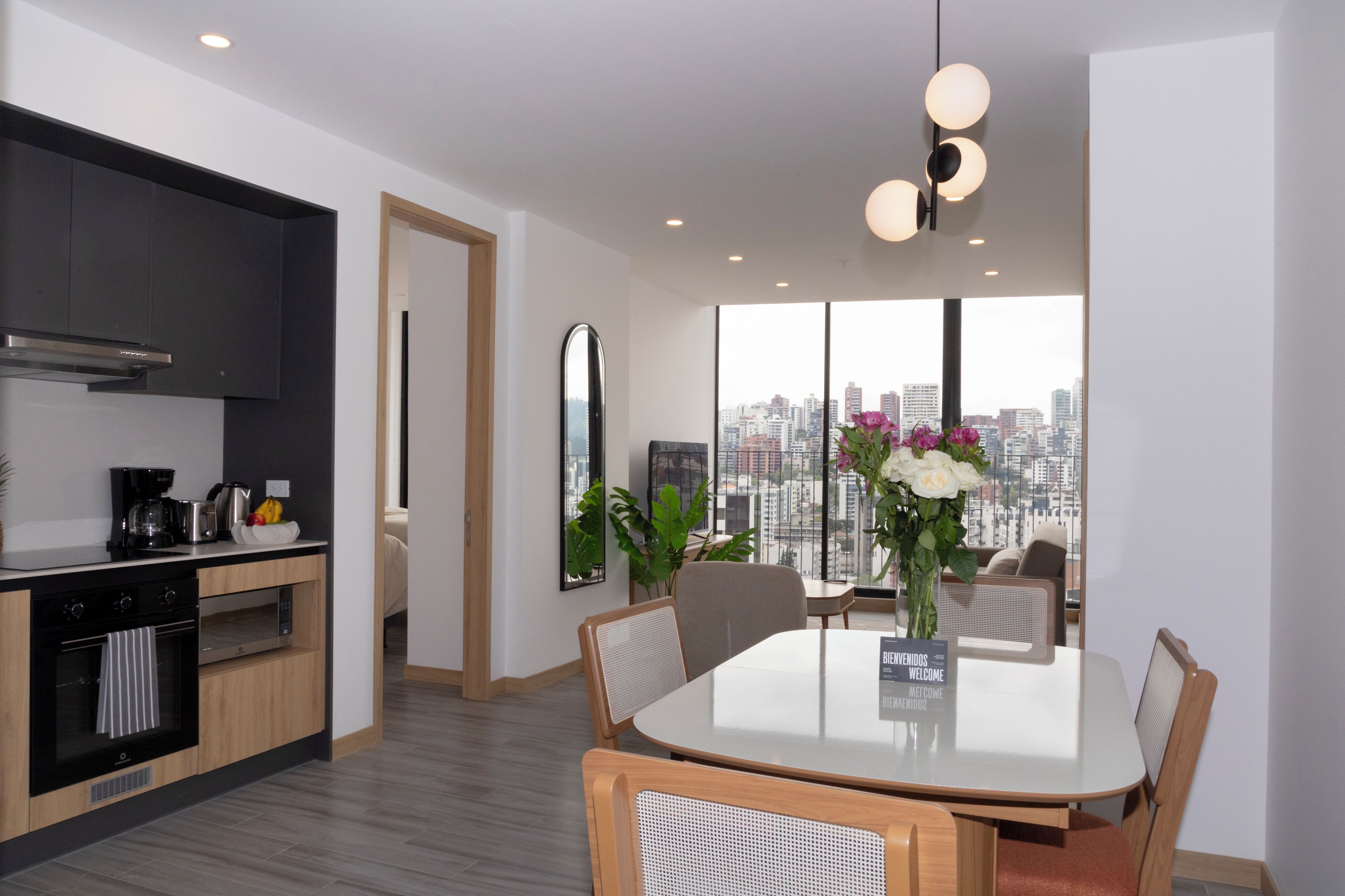Una cocina moderna con comedor, un amplio ventanal con vista a la ciudad y un letrero de bienvenida.