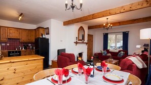 Zona pranzo con tavolo apparecchiato per sei persone, pensili in legno, camino e angolo salotto accogliente con divani rossi.