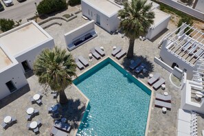 Vista aérea de un hotel moderno con piscina, tumbonas y palmeras.