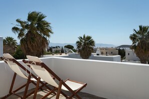 A rooftop terrace with two wooden lounge chairs, white walls, and palm trees. - Soleil Hotel Paros (Drios)