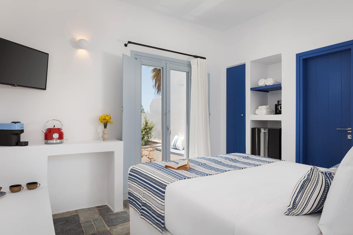 Una habitación de hotel moderna con una cama, un televisor de pantalla plana, una cafetera y una mesita con tazas y fruta.