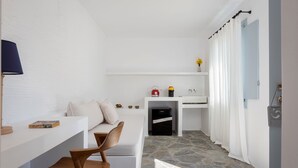 Une pièce moderne et minimaliste avec un sol en pierre, une chaise en bois, un bureau blanc, une petite kitchenette et une salle de bain avec un rideau de douche.