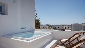 Une terrasse sur le toit avec un jacuzzi, des chaises en bois et une vue sur la mer et les bâtiments.