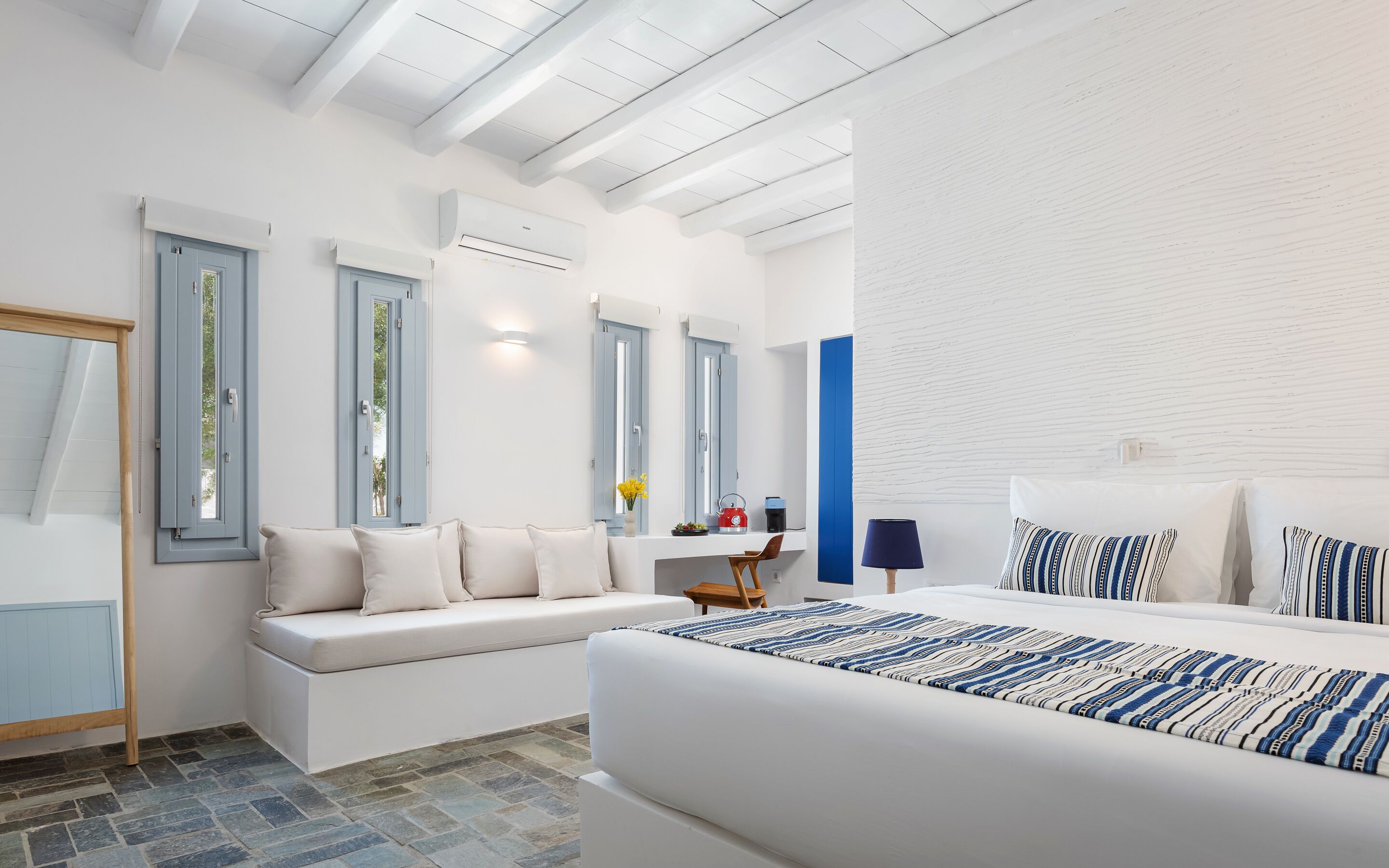Un dormitorio moderno con una cama grande, una zona de estar y un ventanal con contraventanas azules.