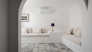 Une pièce au décor minimaliste, avec un canapé blanc, une petite table d’appoint, une lampe et un tableau encadré au mur.