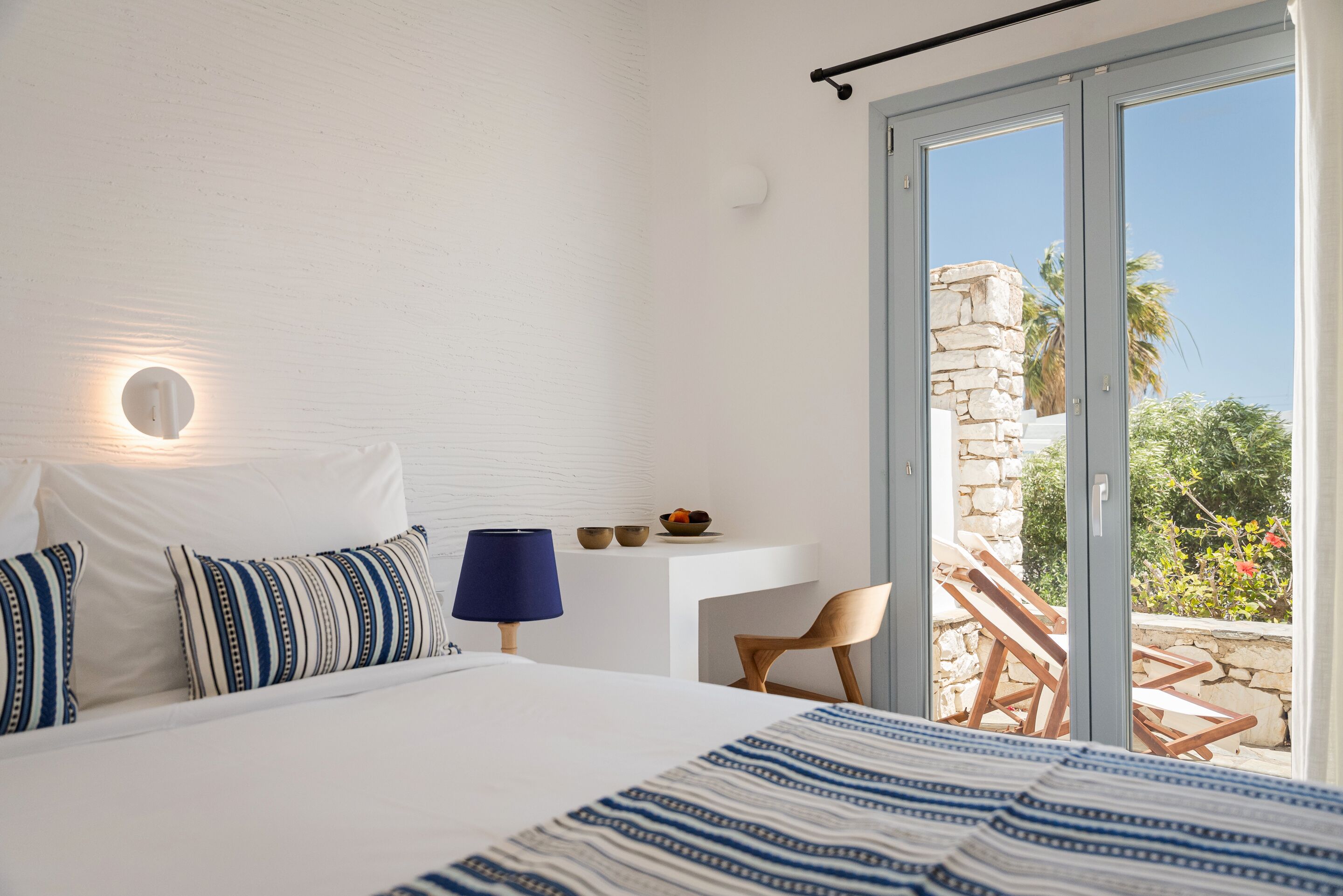 A bedroom with a bed, a desk, a chair, and a view of the outdoors.