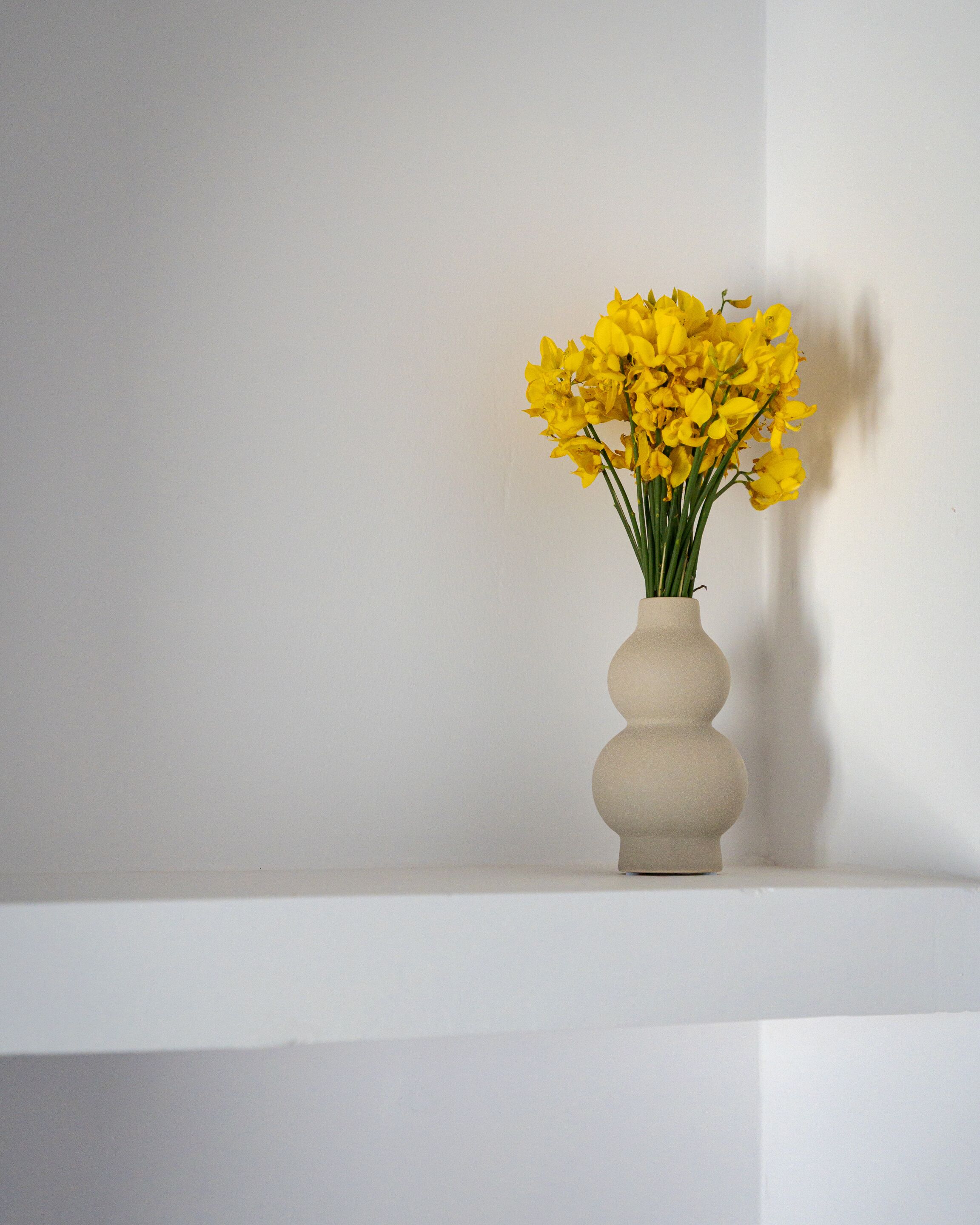 A vase with yellow flowers on a white shelf against a plain wall.