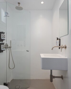 Un baño moderno con cabina de ducha de vidrio, un lavabo blanco y un espejo.