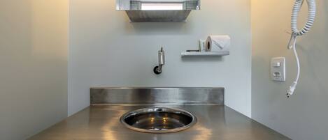 Un baño moderno con lavamanos de acero inoxidable, un espejo, un secador de pelo y un dispensador de toallas.