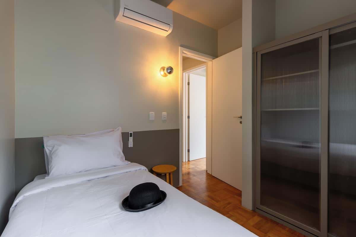 Een hotelkamer met een bed, een klein rond tafeltje, een wandairconditioner en een schuifdeurkast.
