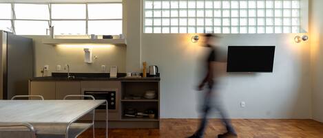 A modern kitchen with a dining area, a TV mounted on the wall, and a large window.