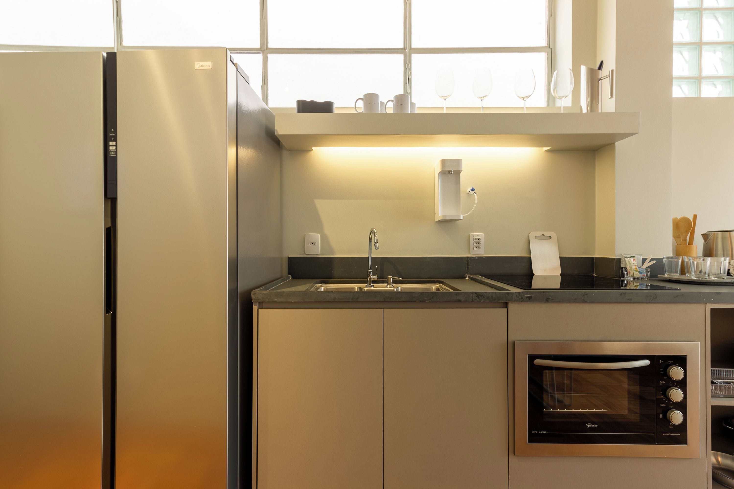 A kitchen with a built-in oven, a stainless steel refrigerator, a sink, and a window above the countertop.