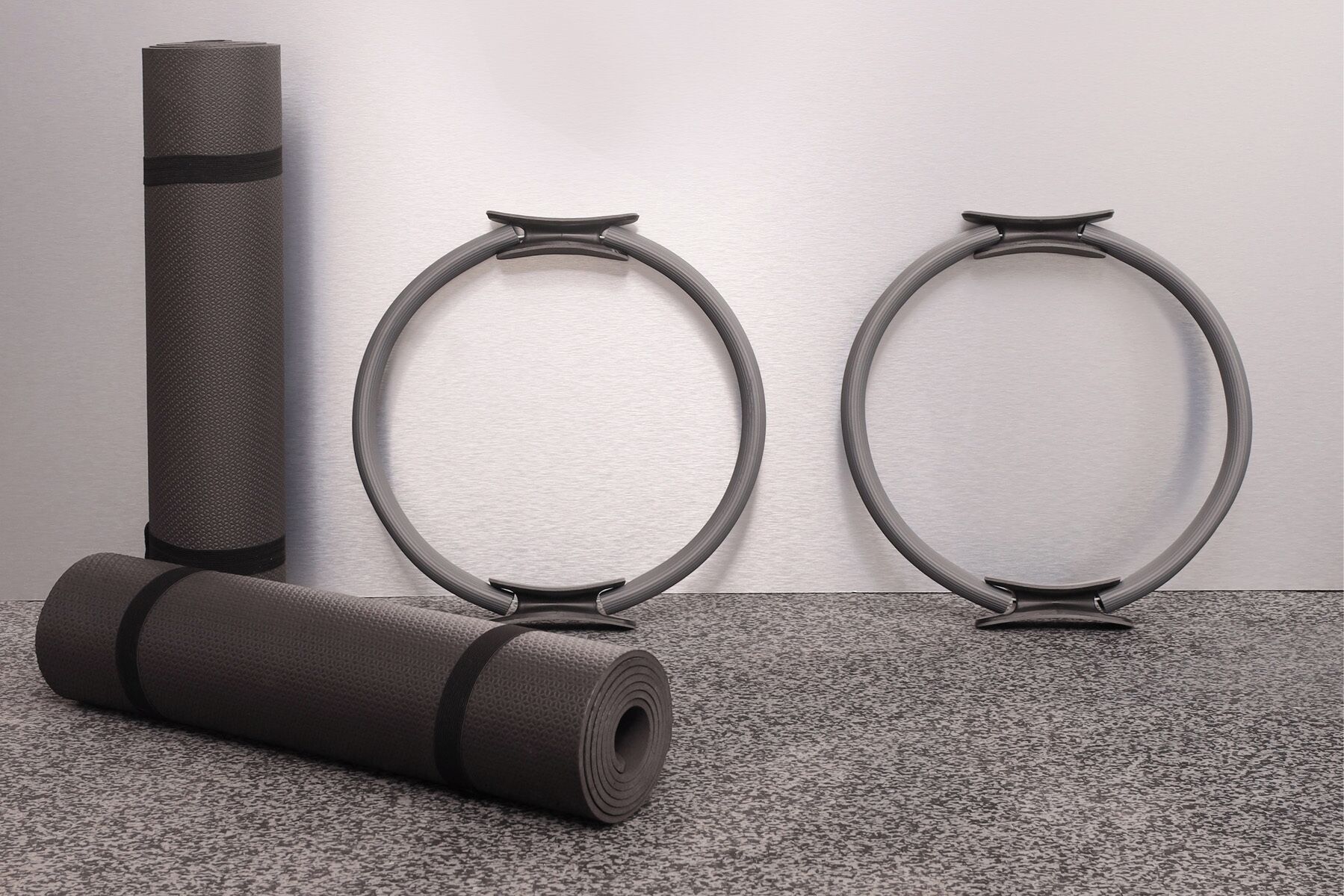 A yoga mat, two exercise rings, and a rolled-up mat on a carpeted floor against a plain wall.